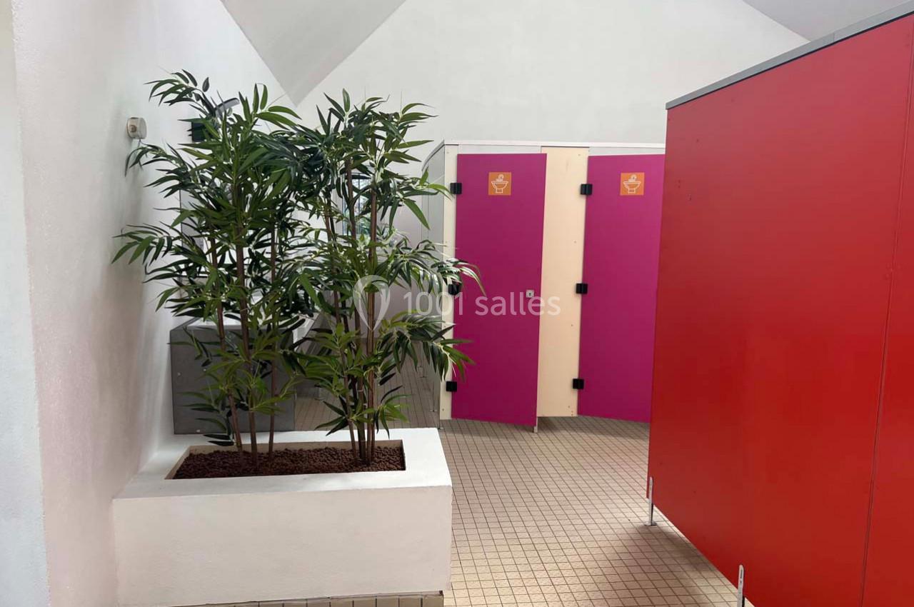Plantes décoratives dans un espace intérieur avec des cabines de toilettes aux portes roses et rouges.