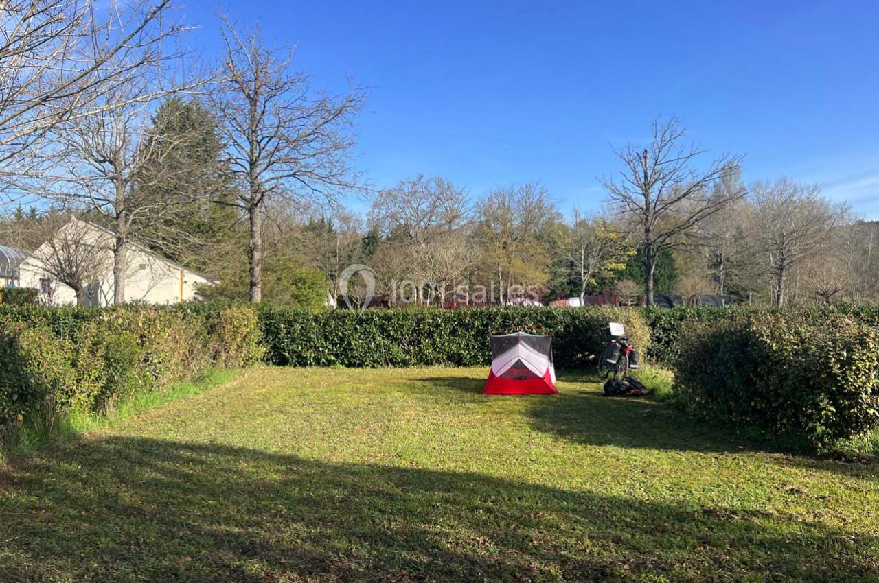 Tente rouge montée sur une pelouse entourée de haies et d'arbres, par une journée ensoleillée.