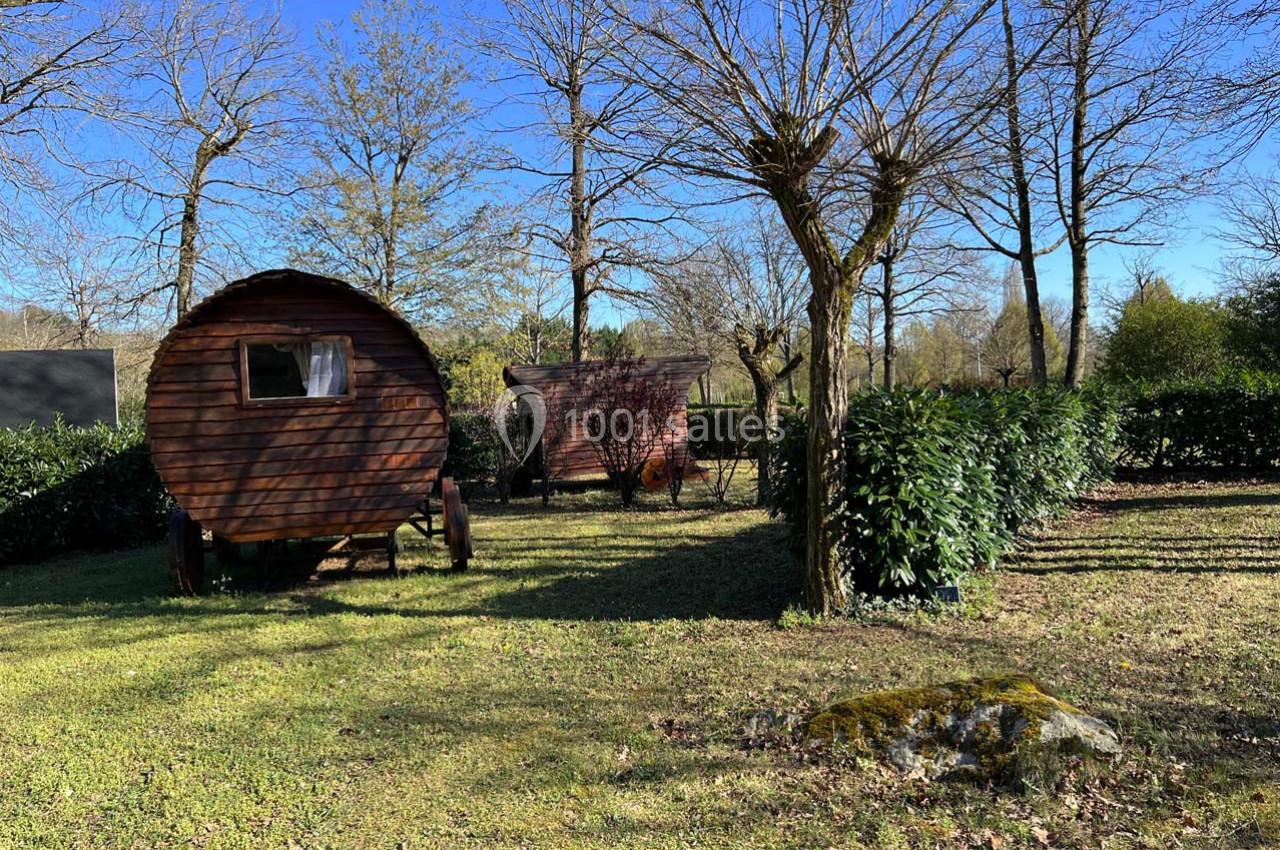 Deux roulottes en bois stationnées dans un espace vert entouré d'arbres et de haies sous un ciel dégagé.