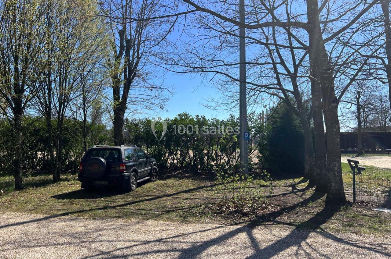 Voiture noire garée sur un espace herbeux près d'arbres, avec un ciel dégagé en arrière-plan.
