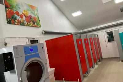 Laverie avec machines à laver, sèche-linge, éviers, miroirs et cabines jaunes dans un espace carrelé.