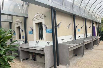 Laverie avec machines à laver, sèche-linge, éviers, miroirs et cabines jaunes dans un espace carrelé.