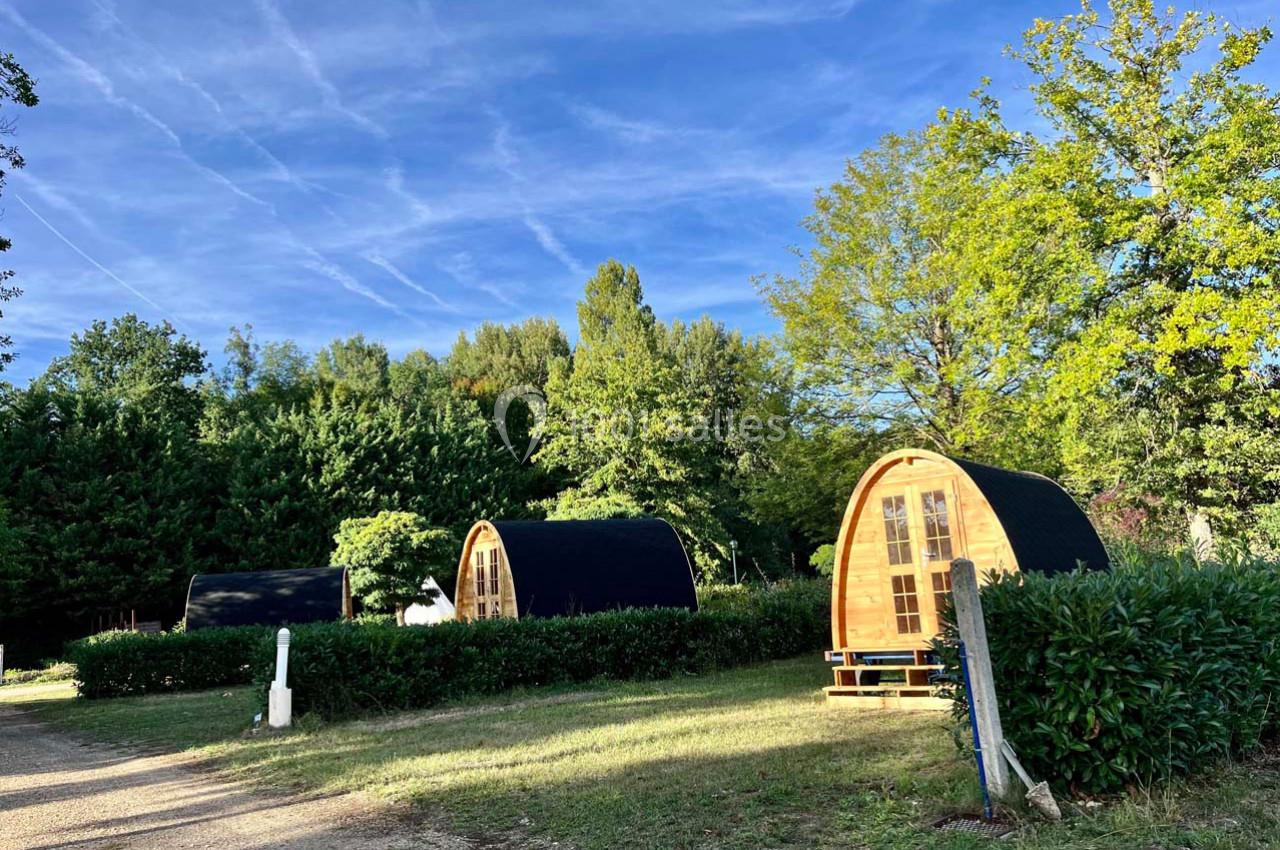 Cabines en bois arrondies dans un cadre verdoyant, entourées d'arbres et d'arbustes sous un ciel bleu.