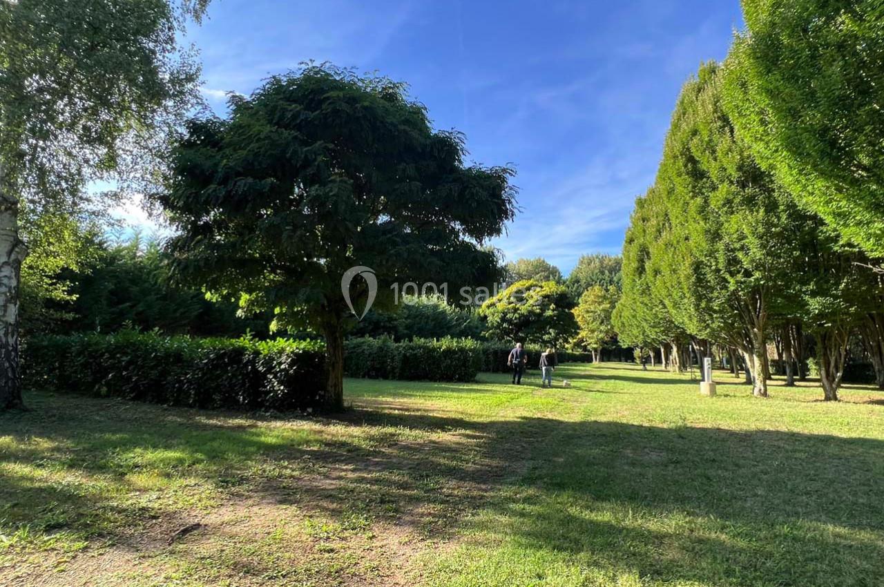 Un parc verdoyant avec des arbres, une pelouse ensoleillée et des personnes marchant au loin.