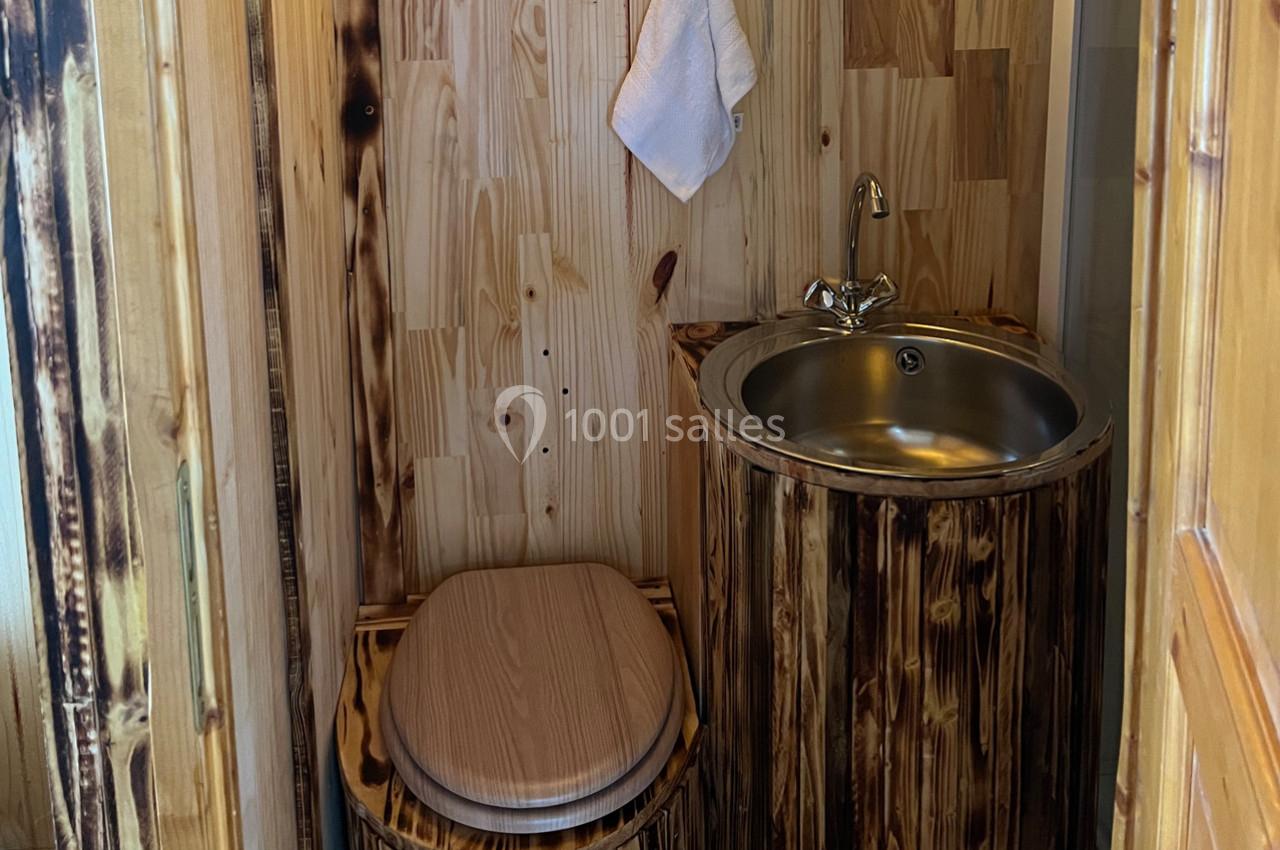 Toilettes en bois avec un lavabo en acier inoxydable intégré dans un meuble assorti, serviette suspendue au mur.