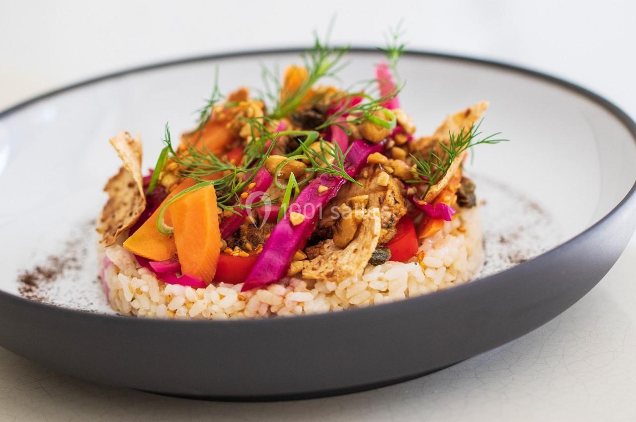 Assiette de riz garnie de légumes colorés, herbes fraîches et morceaux croustillants, présentée dans un bol moderne.