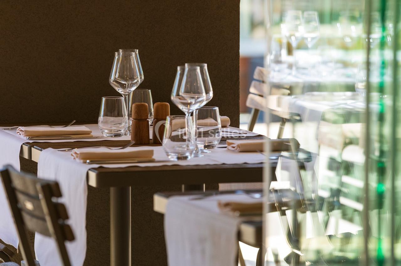 Table de restaurant dressée avec nappes blanches, verres à pied, serviettes et porte-condiments, près d'une baie vitrée.