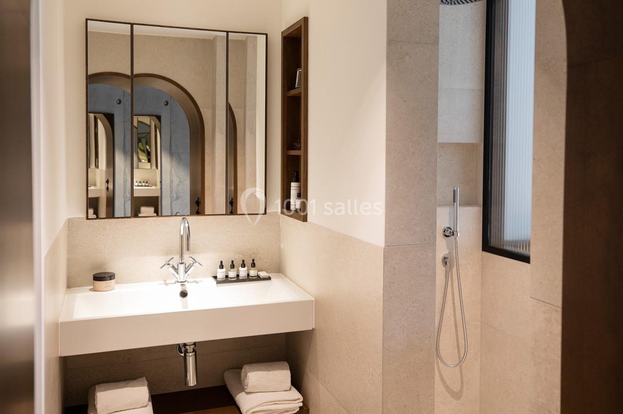 Salle de bain moderne avec lavabo blanc, miroir triptyque, douche à droite et étagères intégrées.
