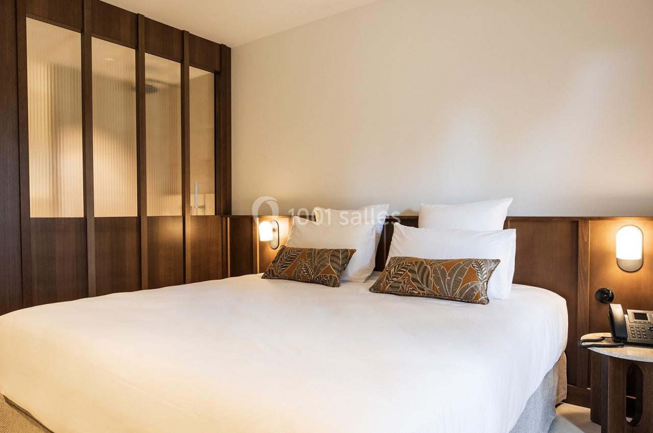 Lit double avec coussins décoratifs dans une chambre lumineuse aux murs clairs et panneaux en bois sombre.