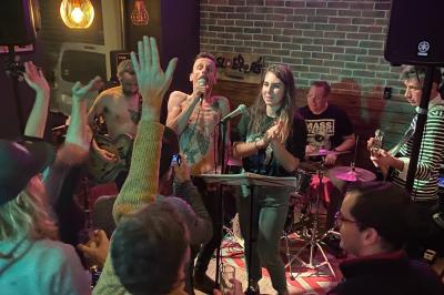 Deux personnes souriantes dans un café à l'ambiance chaleureuse, avec un mur en briques et une enseigne néon.