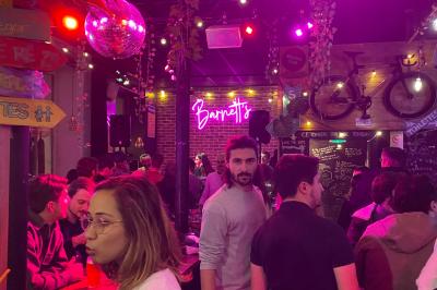 Deux personnes souriantes dans un café à l'ambiance chaleureuse, avec un mur en briques et une enseigne néon.