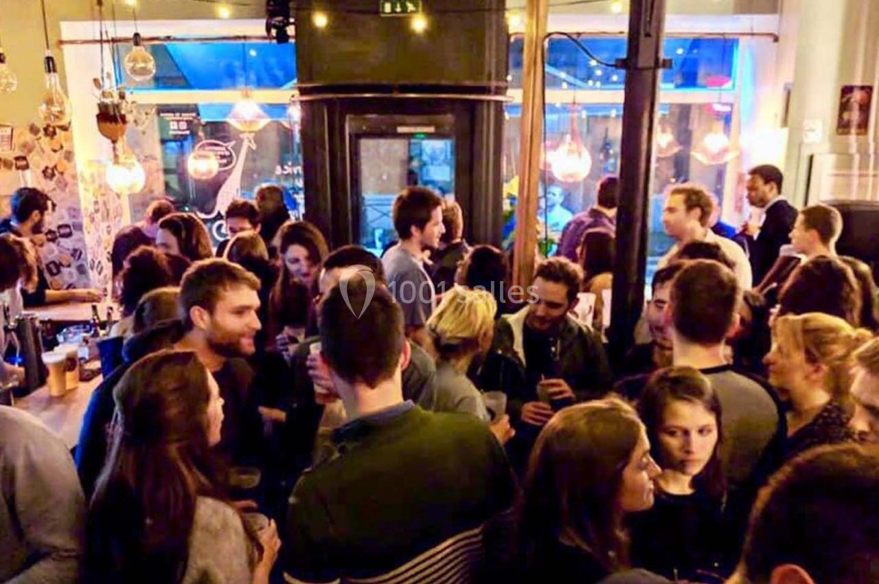 Groupe de personnes discutant et partageant des boissons dans un bar animé avec une ambiance chaleureuse.