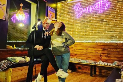 Deux personnes souriantes dans un café à l'ambiance chaleureuse, avec un mur en briques et une enseigne néon.