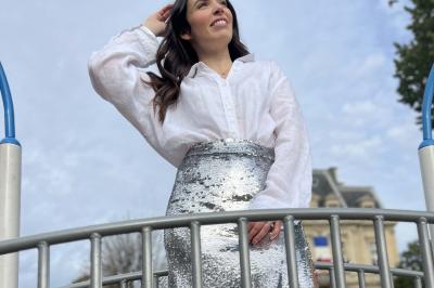 Miniature Pretty Women #5 Femme souriante portant une jupe argentée scintillante et une chemise blanche, debout sur une structure métallique en…