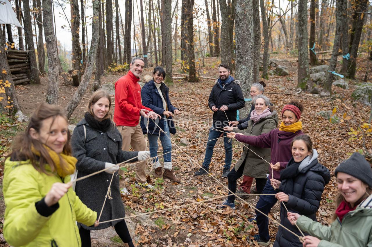 Un groupe de personnes participe à une activité collaborative avec des cordes dans une forêt en automne.