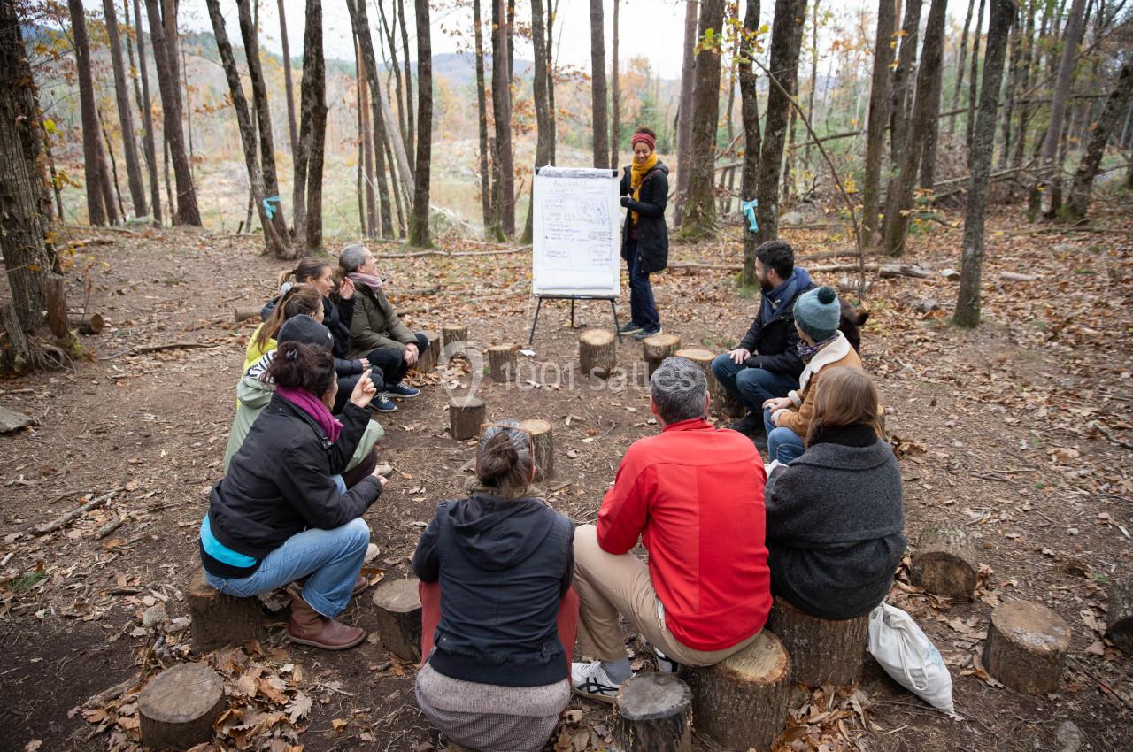 Un groupe de personnes assises en cercle sur des rondins de bois écoute une présentation en forêt.