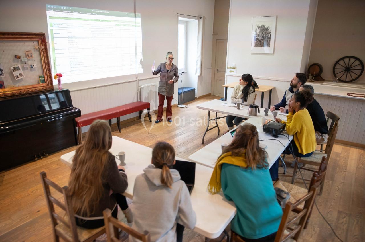 Une personne donne une présentation devant un groupe assis autour de tables dans une salle lumineuse.