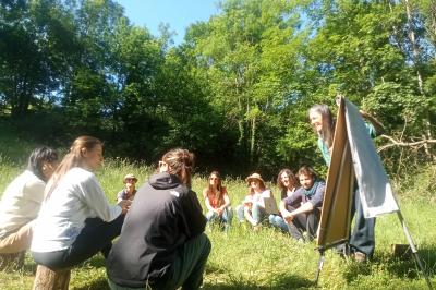 Salon chaleureux avec fauteuils en rotin, canapé, poêle à bois, bibliothèque et lumière naturelle.