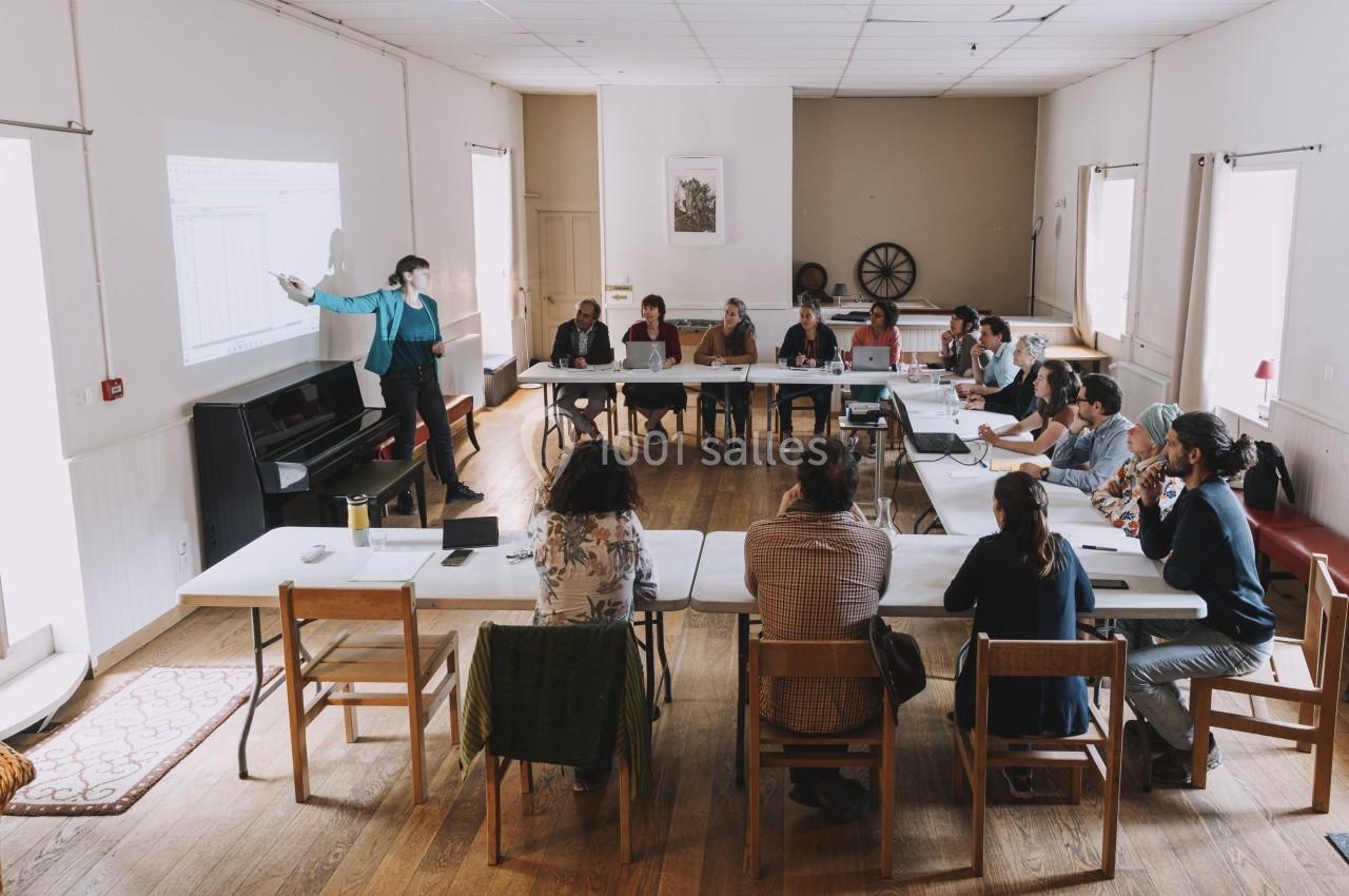 Une personne présente un graphique projeté à un groupe de personnes assises autour de tables dans une salle lumineuse.