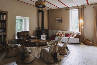 Salon chaleureux avec fauteuils en rotin, canapé, poêle à bois, bibliothèque et lumière naturelle.