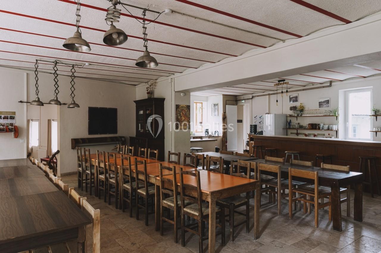 Salle à manger spacieuse avec de longues tables en bois, des chaises alignées et un bar en arrière-plan.
