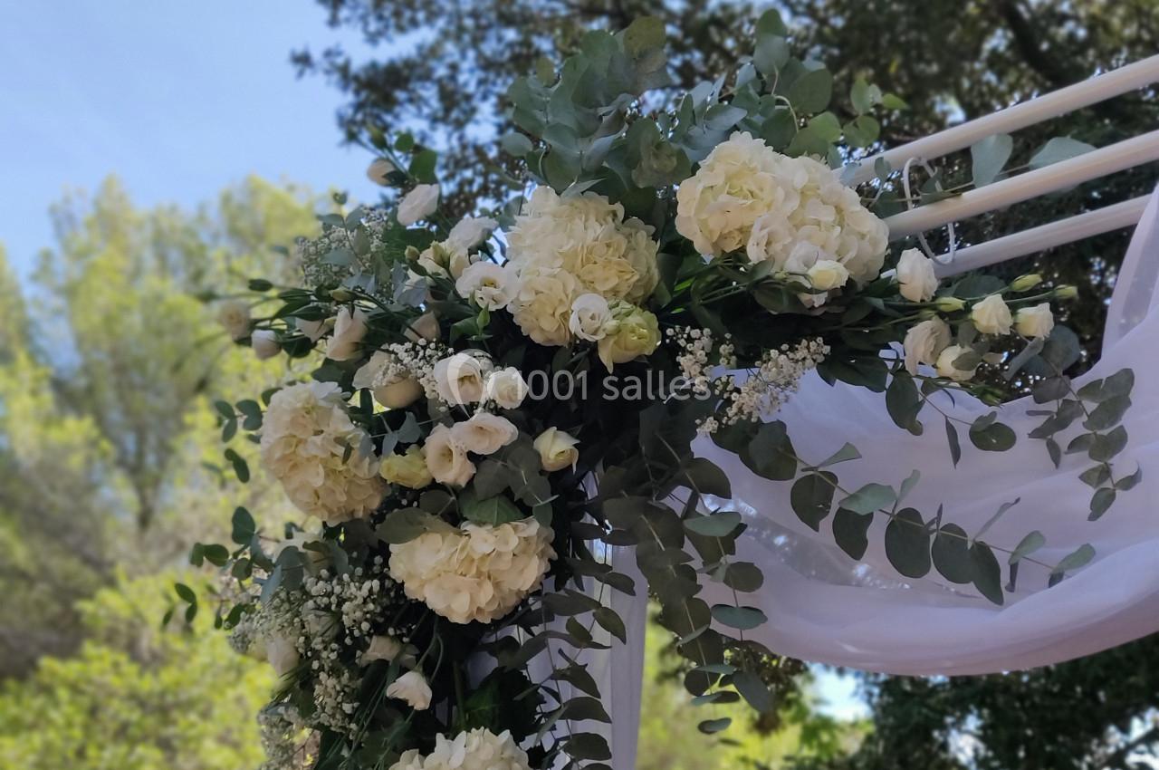 Arrangement floral blanc et vert avec des roses et hortensias décorant une arche en bois sous un ciel dégagé.