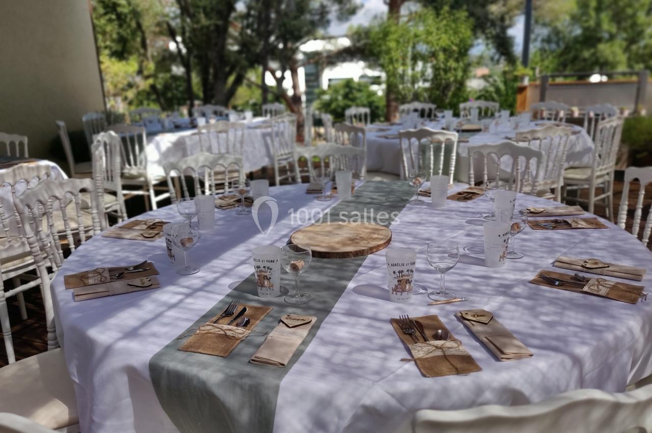 Table ronde dressée pour un événement en extérieur, avec nappes blanches, chemins de table gris et couverts disposés.