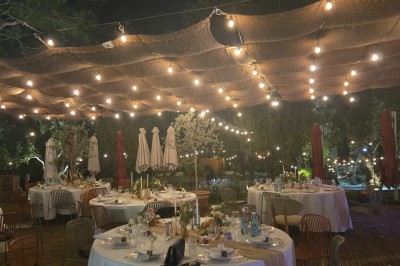 Décoration de table élégante sous un plafond de guirlandes lumineuses et de toile de jute en soirée extérieure.
