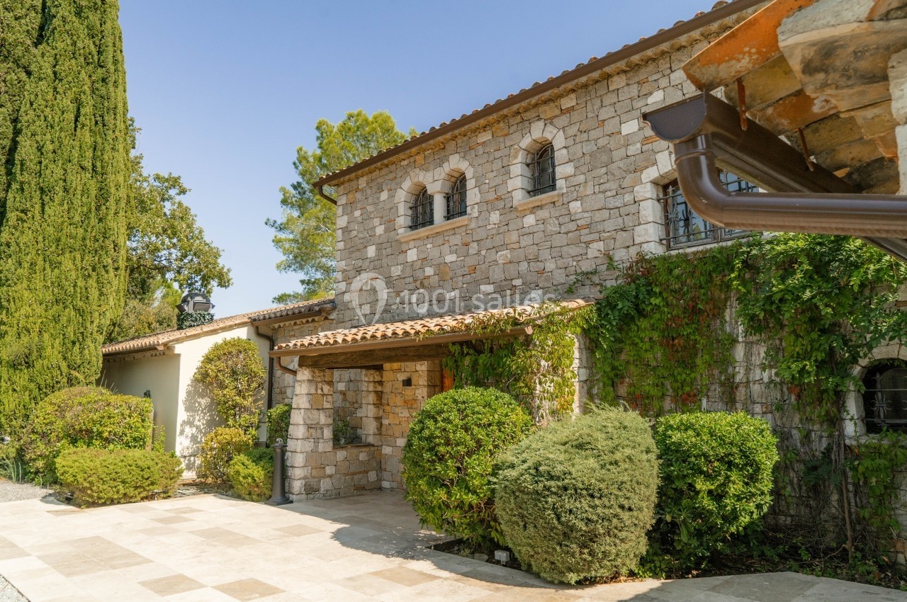 Façade en pierre d'une maison traditionnelle entourée de végétation avec une allée pavée au premier plan.