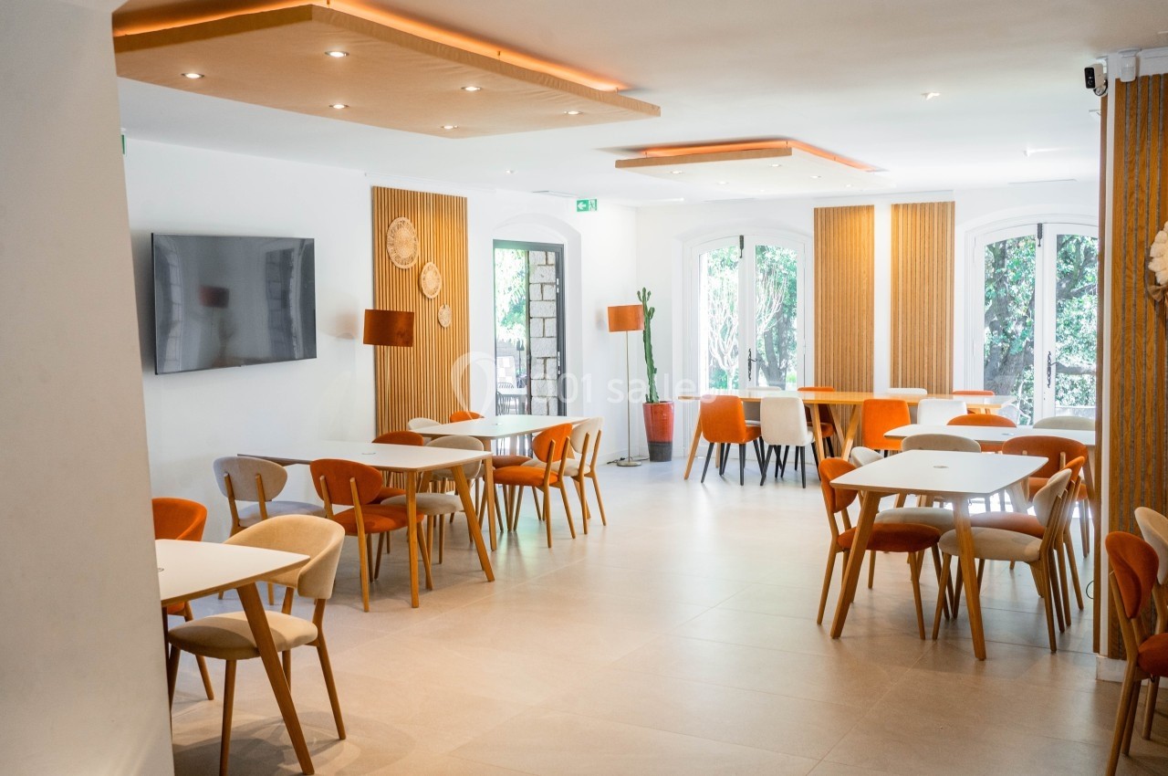Salle lumineuse avec tables et chaises colorées, décorée de panneaux en bois et d'une télévision murale.