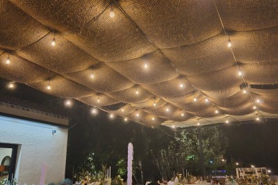 Décoration de table élégante sous un plafond de guirlandes lumineuses et de toile de jute en soirée extérieure.