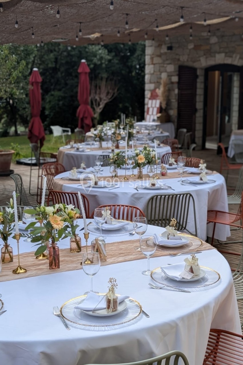 Tables rondes décorées pour un événement en extérieur, avec nappes blanches, fleurs et vaisselle élégante.