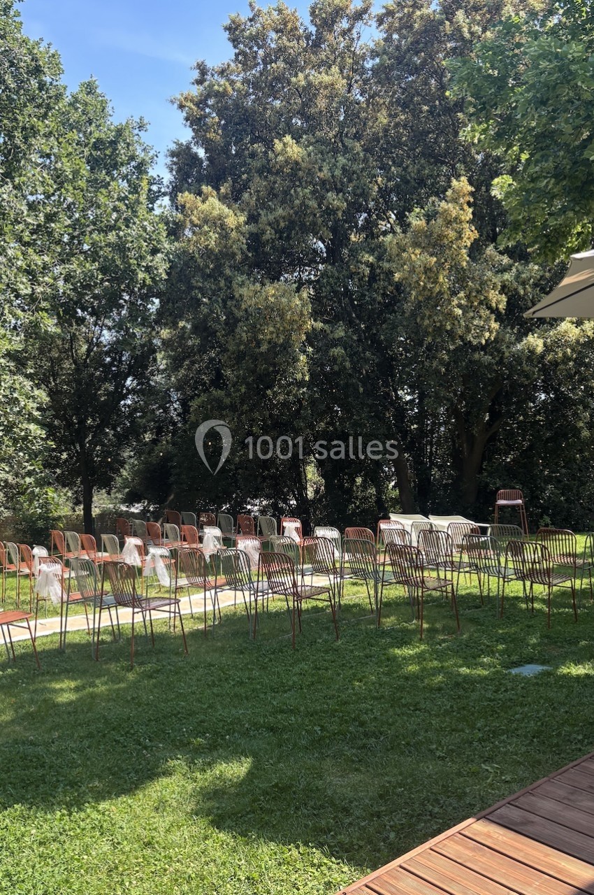 Chaises alignées sur une pelouse verte, disposées pour un événement en plein air, entourées d'arbres et de lumière naturelle.