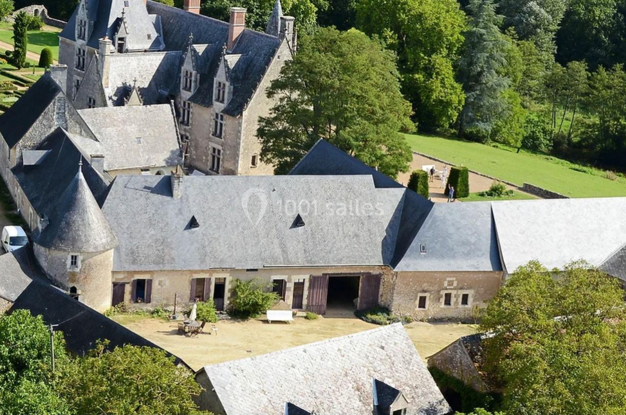 Vue aérienne d'un manoir ancien entouré de bâtiments annexes, avec un jardin et des arbres en arrière-plan.