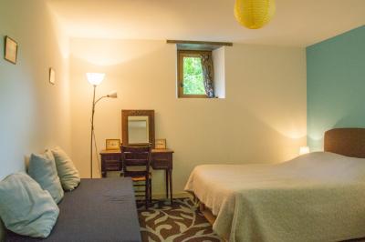 Chambre lumineuse avec un lit double, un canapé, un bureau en bois et une fenêtre donnant sur un espace vert.