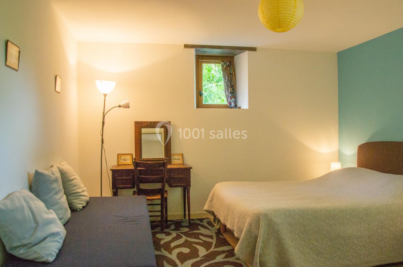 Chambre lumineuse avec un lit double, un canapé, un bureau en bois et une fenêtre donnant sur un espace vert.