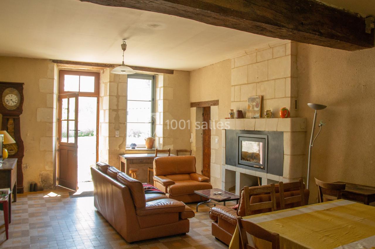 Salon lumineux avec murs en pierre, cheminée, mobilier en bois et canapés en cuir, donnant sur un jardin par une porte…