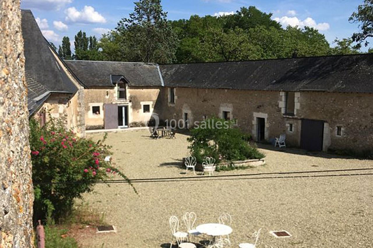 Cour intérieure d'une ancienne ferme avec bâtiments en pierre, mobilier de jardin blanc et végétation.