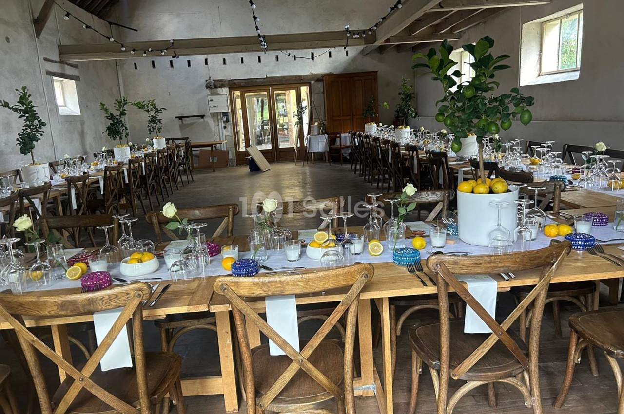 Salle de réception décorée avec des tables en bois, vaisselle élégante, citrons et fleurs blanches, prête pour un événement.