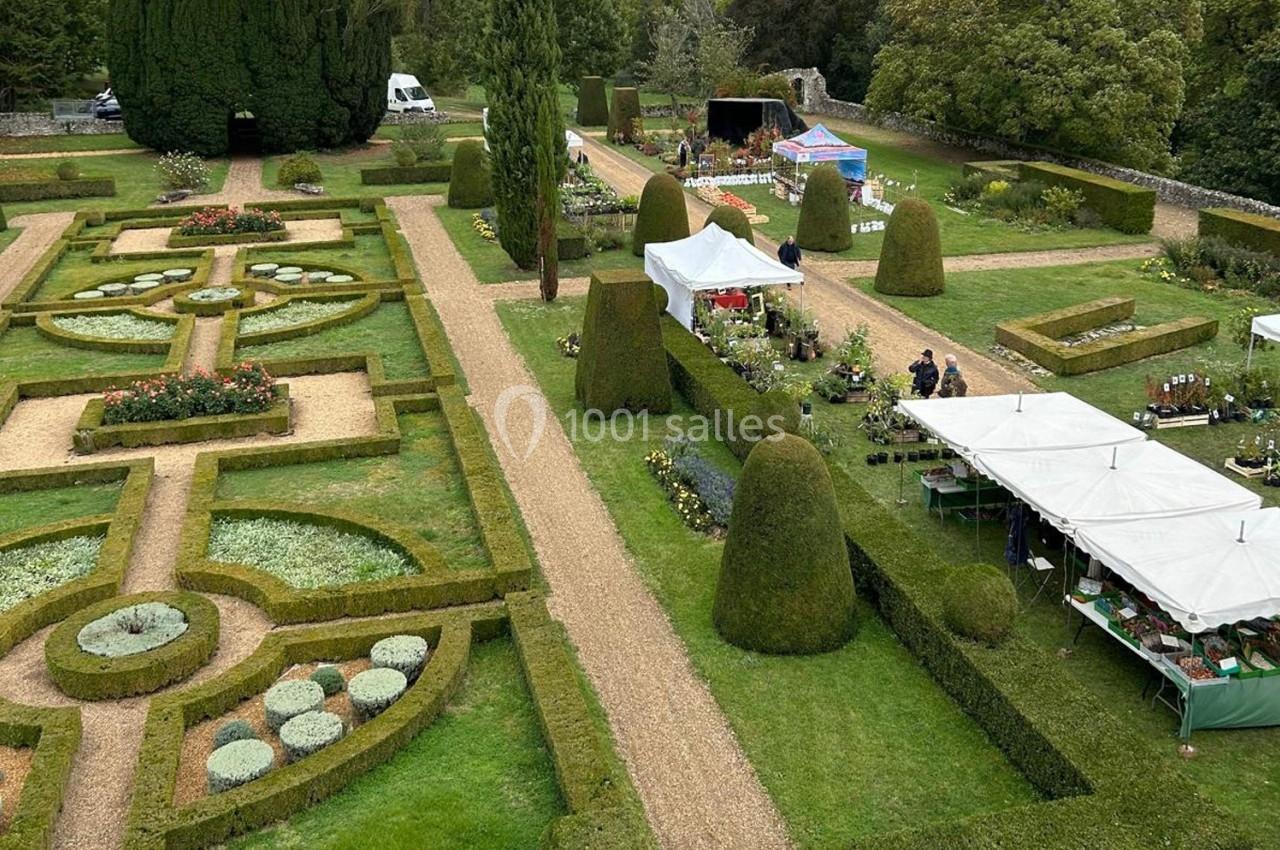 Jardin à la française avec allées gravillonnées, parterres géométriques et stands de marché en arrière-plan.