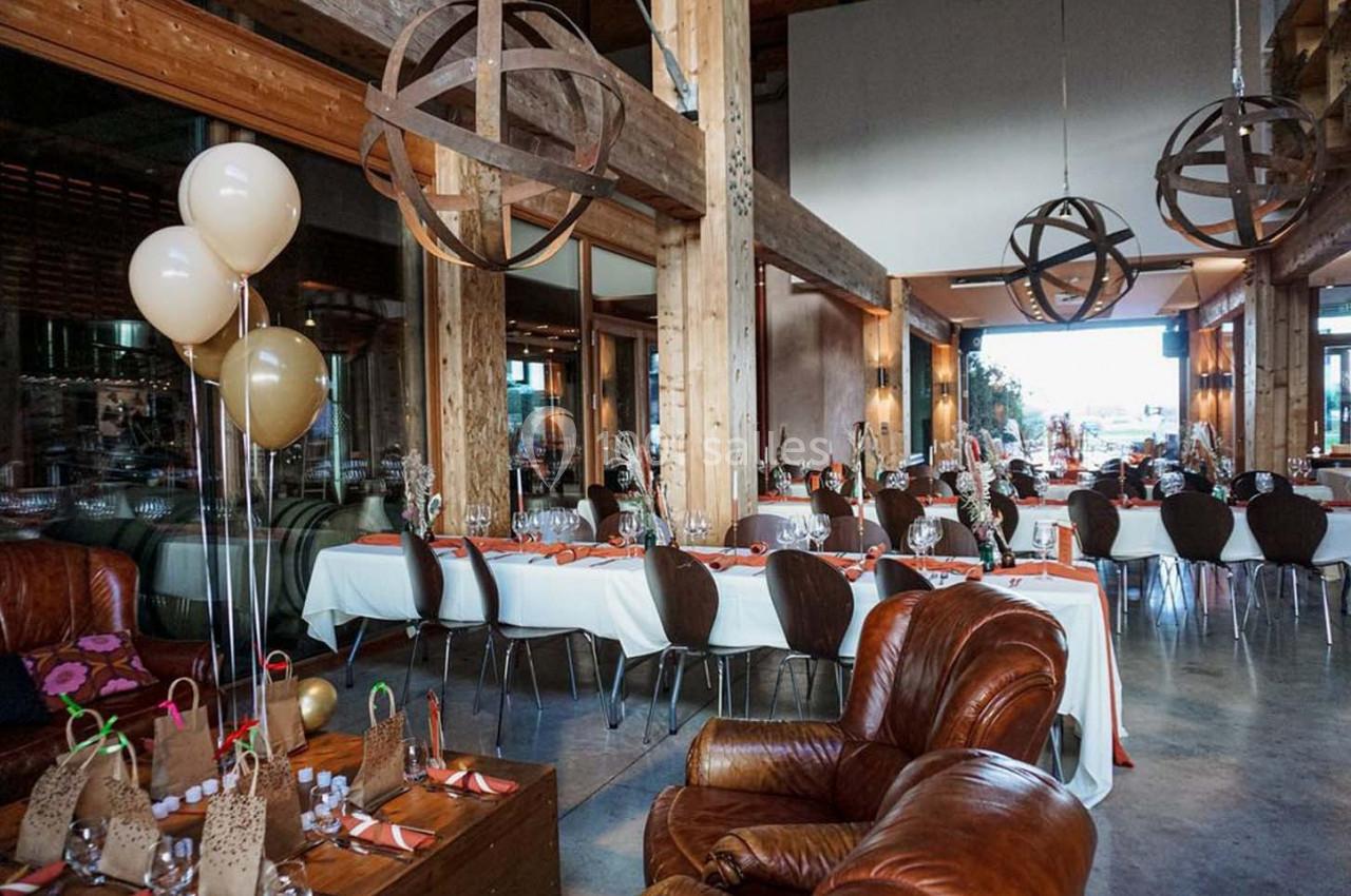 Salle de réception lumineuse avec tables dressées, décorations en bois et ballons beige et doré.