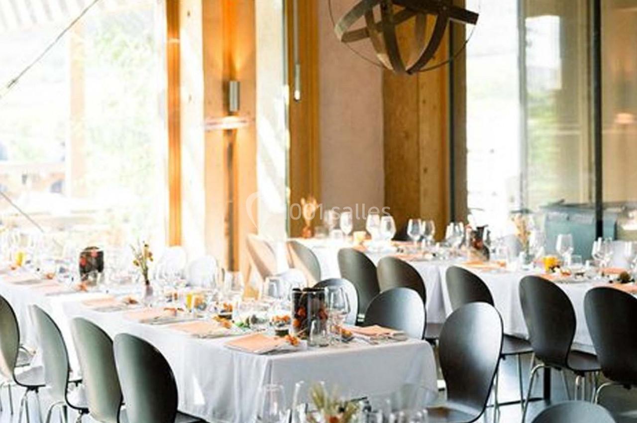 Salle lumineuse avec tables dressées, nappes blanches, chaises modernes et décoration élégante pour un repas.
