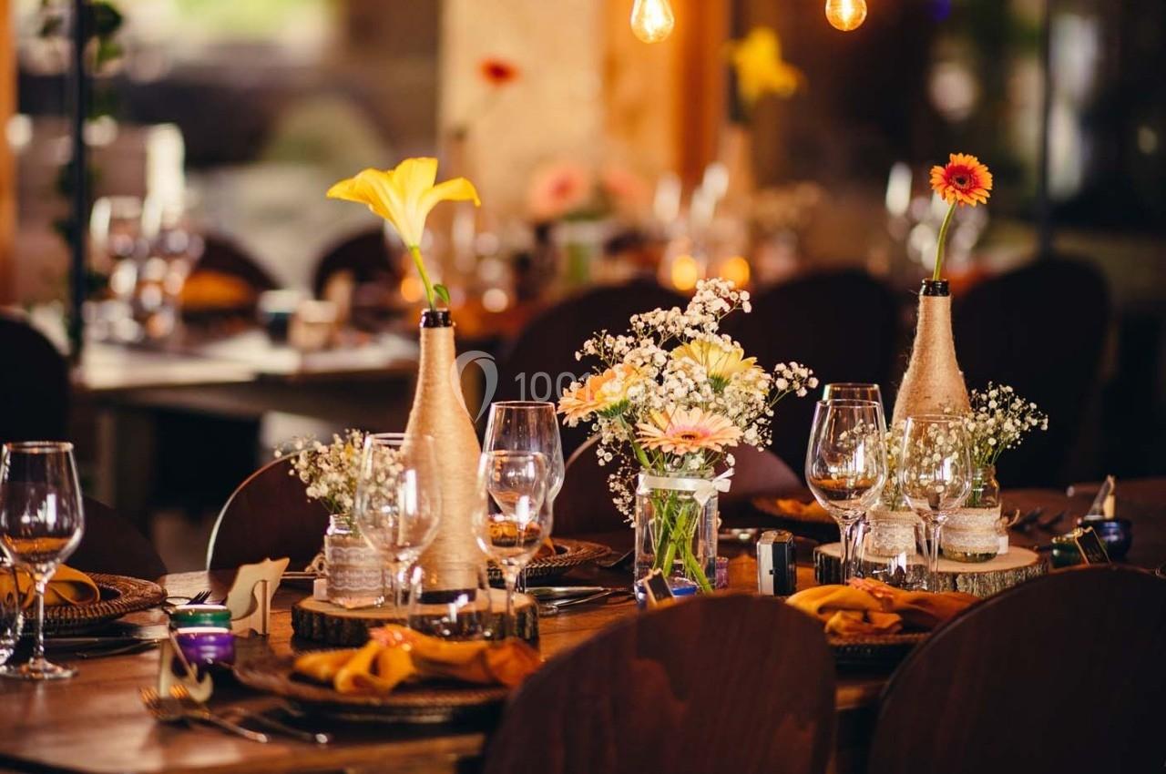 Table décorée avec des fleurs, des verres à pied et des assiettes, dans une ambiance chaleureuse et lumineuse.