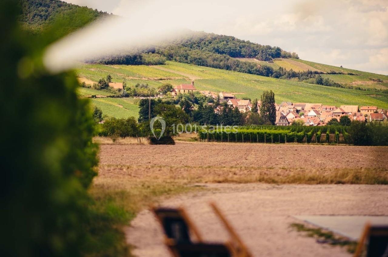 Village entouré de vignes et de collines verdoyantes sous un ciel partiellement nuageux.