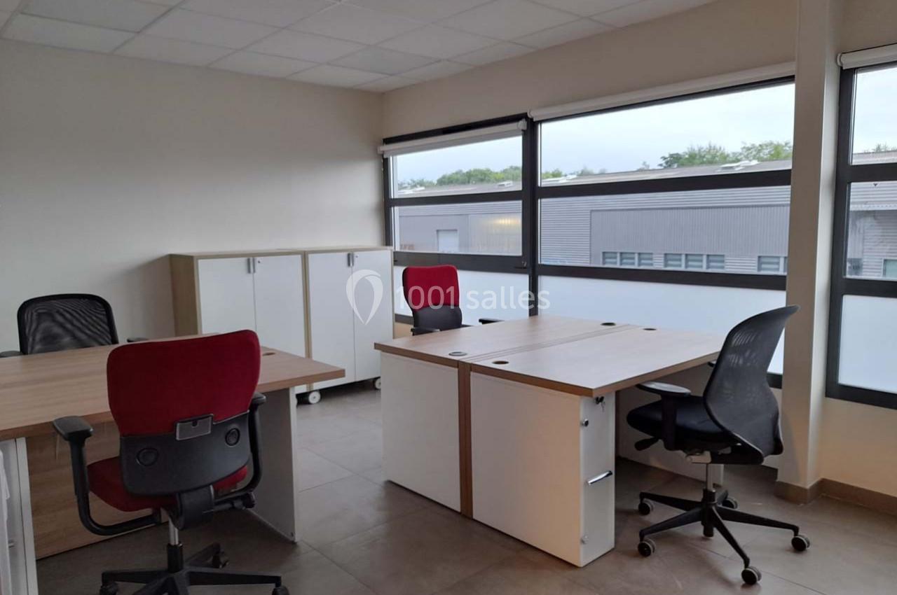 Bureau lumineux avec trois postes de travail équipés de chaises, rangements et grandes fenêtres donnant sur l'extérieur.