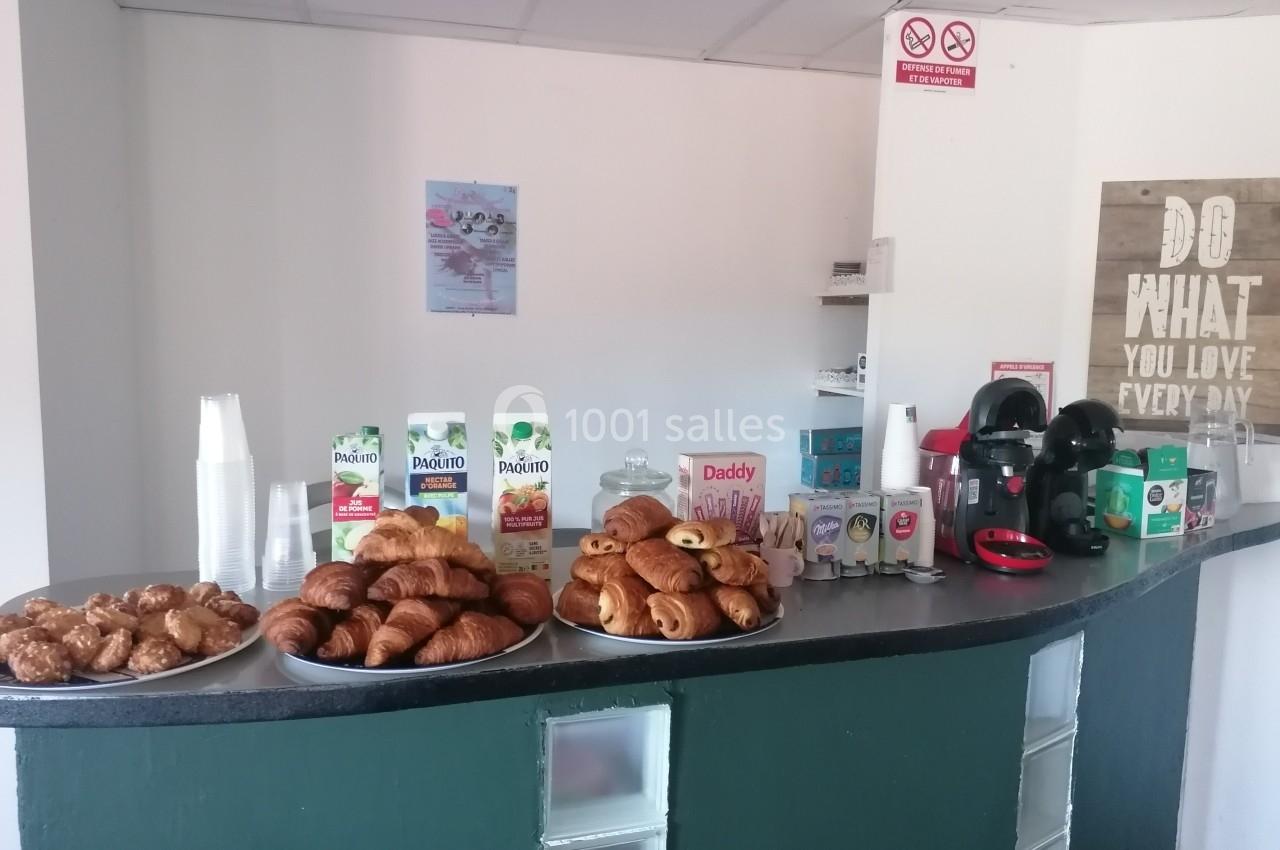 Buffet avec viennoiseries, jus de fruits, café et accessoires sur un comptoir dans un espace lumineux.