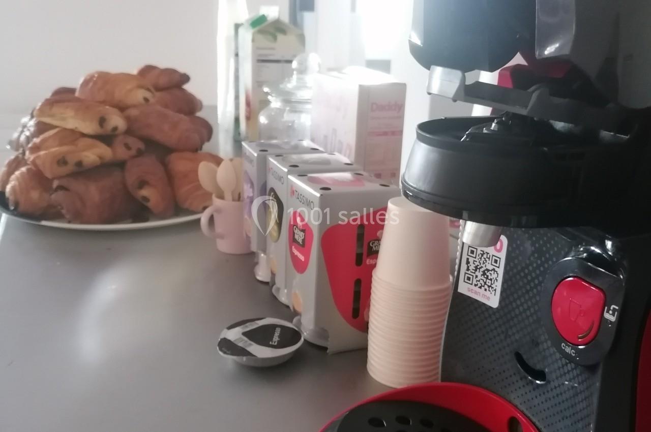 Machine à café rouge et noire sur un comptoir, avec des viennoiseries et des boîtes de capsules en arrière-plan.