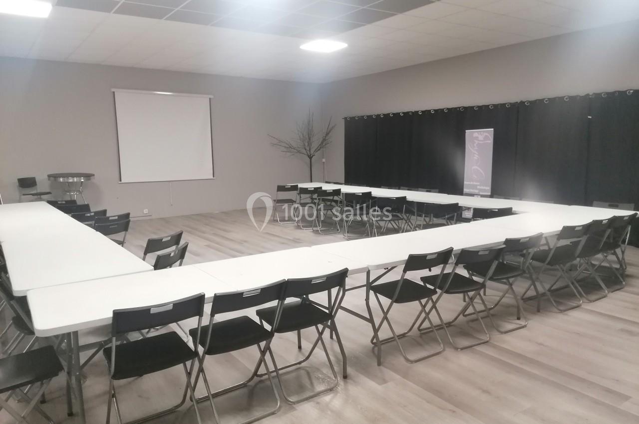 Salle de réunion avec des tables disposées en U, des chaises pliantes noires et un écran de projection au fond.