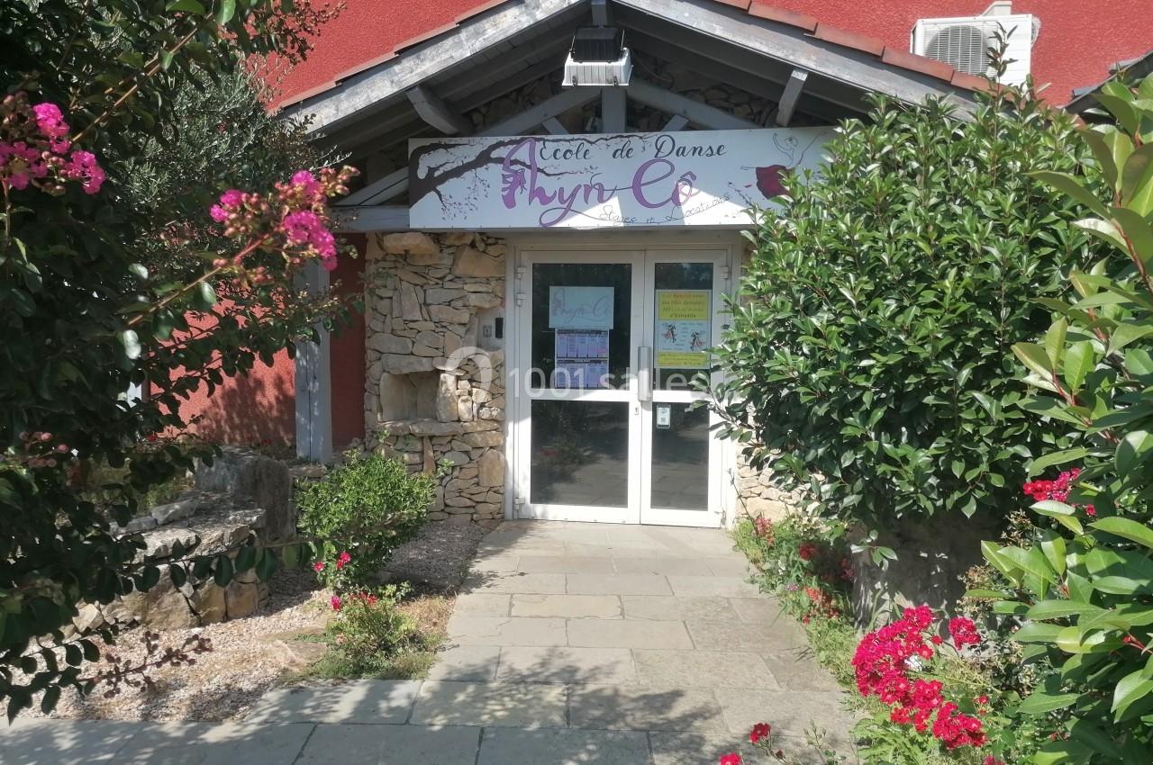 Entrée d'une école de danse avec une porte vitrée, entourée de plantes et de fleurs colorées.