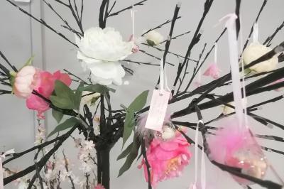 Arbre décoratif avec branches noires ornées de fleurs artificielles et de petites décorations suspendues.